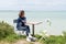 Single woman relaxing on promenade with smartphone on seaside coast beach view