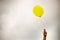 single yellow balloon under cloudy sky. hand holds the balloon rope up to the sky.