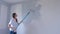 Single young woman is painting wall in gray using paint rollers in new flat.