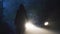 A sinister hooded figure standing in front of a car. On a spooky forest road on a foggy evening