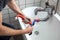 The sink pipe is being fixed by a male plumber in overalls, as seen from a high angle, providing a clear view of his workmanship