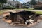 a sinkhole in a residential neighborhood, with pieces of broken furniture and debris visible inside