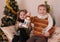 Sister and brother in knitted clothes under golden Christmas tree