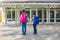 Sister and brother return to school after vacation. Children hold hands in front of school doors. The new school year