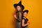 Sisters girls in witches costumes with ignited candles or burning candles and looking at camera on yellow background.