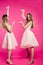 Sisters in pink dresses emotionally posing and pointing by hands.