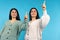Sisters pointing with index fingers up. Caucasian twins in same casual clothes on blue background
