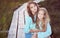 Sisters relaxing outdoors while sitting on a wooden path in a field at sunset.