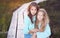 Sisters relaxing outdoors while sitting on a wooden path in a field at sunset.