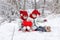 Sisters twins with heart in the hands are sitting on the snowy ground