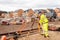 Site engineer in hi-viz working on house building construction site using modern surveying equipment against new houses