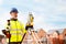 Site engineer in hi-viz working on house building construction site using modern surveying equipment against new houses nad blue