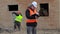 Site manager with documentation and worker in background near building