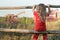 Sitting girl observing farm field with red working combine harvester