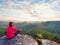 Sitting hiker on rock. Man in red black warm clothes is sitting on cliff and enjoying far view.