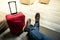 Sitting with the red suitcase in the airport waiting room. Detail of the feet and luggage. Above photography