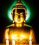 Sitting statue of smiling buddha with lighted candles. Golden buddha glowing holy colorful light.