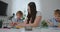 Sitting at the table in the living room, a young mother teaches her son to hold a pencil and teaches to draw