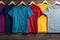 Six colorful t-shirts hanging on hangers on brown background.