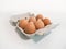 Six eggs in a carton on a white table, angled view.