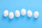 Six fresh white farm eggs lined up in a row on blue background