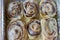 Six frost cinnamon rolls in an aluminum foil baking pan.