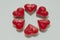 Six heart shaped red candles form flower on white background.