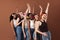 Six laughing women with flowers in hair. Multi-ethnic group of females raises hands up over brown background