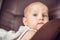 A six-month-old blue-eyed baby in a white lace dress sits in a brown leather chair at home