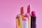 Six old used lipstick tubes stand on a pink background