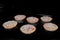 Six uncooked homemade mini pizzas on tray in electric oven, black background