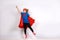 Six year blonde girl dressed like superhero having fun at home. White wall on background