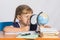 Six-year girl sitting at table and looks at the globe through a magnifying glass