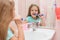 Six year old girl cleans the lower front teeth look in the mirror in the bathroom