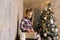 Six-year-old girl in a plaid dress on the background of a Christmas tree opens her new year gift