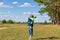 A six-year-old preschooler boy in a blue jacket launches a toy plane in a field against a blue sky with clouds on a summer day