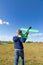 A six-year-old preschooler boy in a blue jacket launches a toy plane in a field against a blue sky with clouds on a summer day