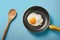 Sizzling fried eggs in pan, wooden spoon centerpiece, blue background
