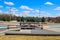 A skate park with young men riding skateboards surrounded by yellow winter grass, green umbrellas over benches