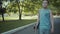 Skateboarder walks in a park with a skateboard in hands.