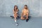 Skateboarding. Couple In Casual Outfit Sitting On Skateboards Against Concrete Wall At Skatepark