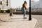 Skateboarding Woman In The City. Skater girl in denim is riding her board on the square. Athletic Woman skateboarder. Building on