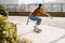 Skateboarding Woman In The City. Skater girl in denim is riding her board on the square. Athletic Woman skateboarder. Building on