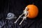 Skeleton, orange pumpkin, and a skeleton pattern face mask on a black velvet background