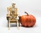 Skeleton sitting in an Adirondack chair with an orange pumpkin  on white