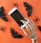 Skeleton using smartphone. Bats and spiders on orange  background