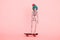 skeleton wearing knitted hat riding skateboard against pastel pink background