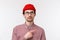 Skeptical good-looking young hipster guy in red beanie and check shirt, glasses, peeking doubtful, looking pointing