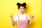 Skeptical teenage asian girl with glam pink makeup, pointing and looking up unamused, standing reluctant on yellow