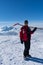 Ski patroller on snow caped mountain is standing against sun with a red rescue jacket and a shovel on his shoulders